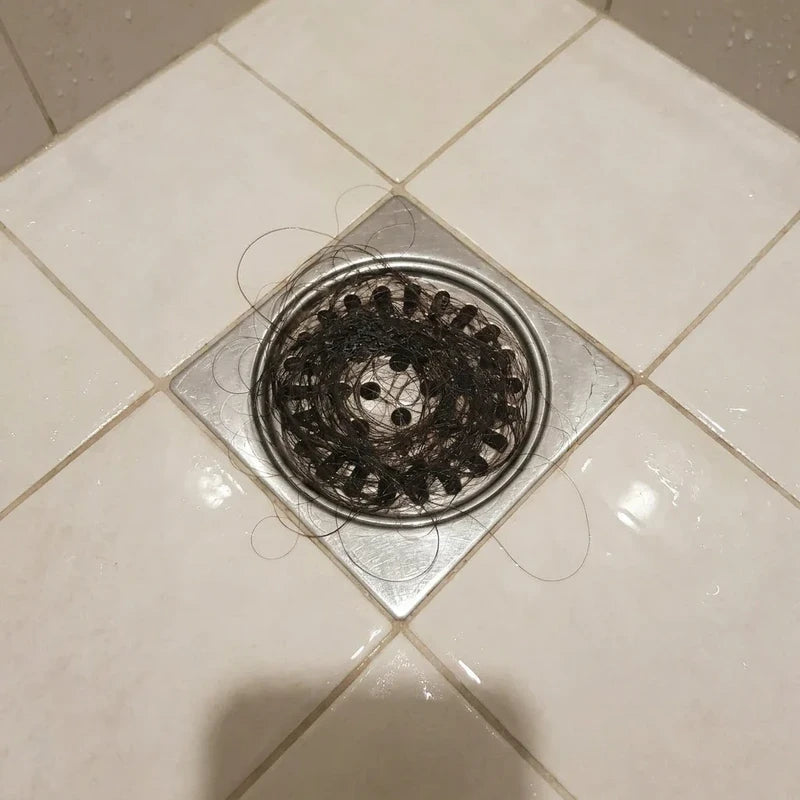 Cheveux accumulés autour de la bonde d’une douche carrelée.